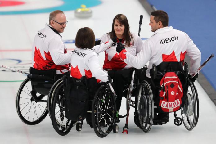 Four wheelchair curling athletes form a circle on the ice